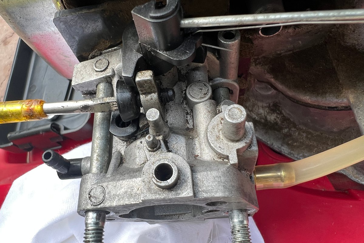 Turning the air screw to adjust the air to fuel ratio on a lawn mower carburetor