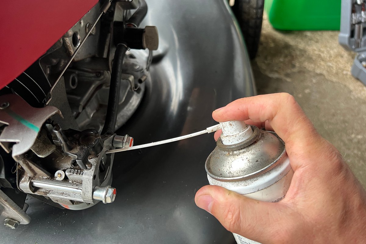 spraying aerosol carb cleaner into lawn mower carburetor to clean it and help it run more smoothly 