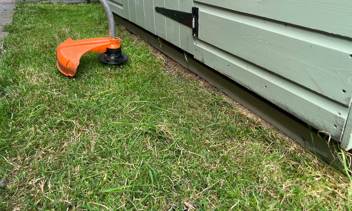string trimmer cutting grass around shed